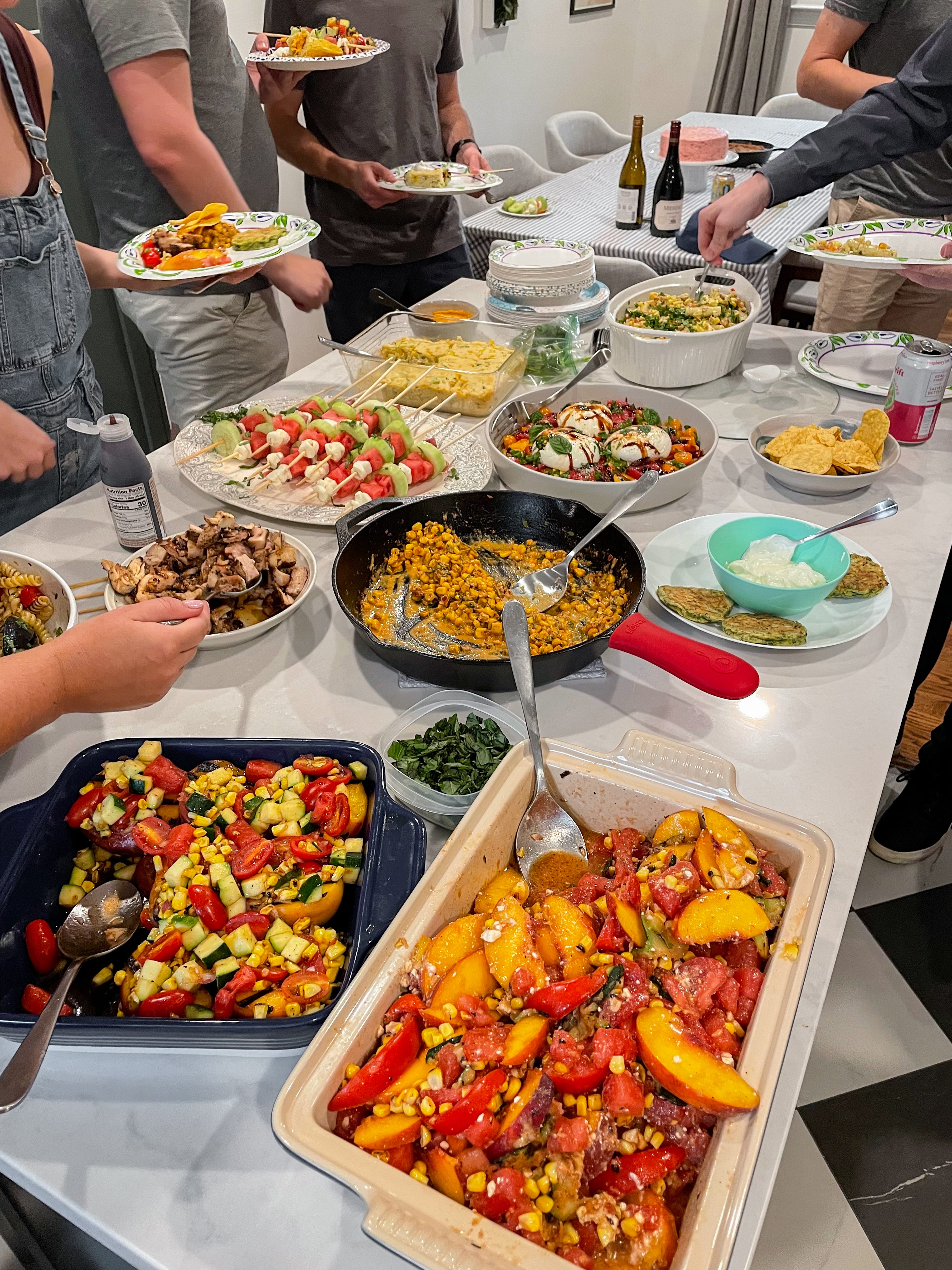 Platters of fruit and vegetable dishes on a table from a summer produce party.