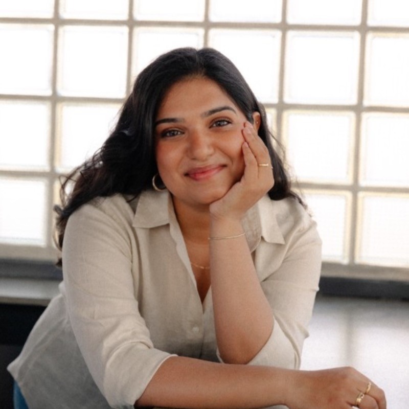 Nupur Amin Marquardt smiling leaning on a counter looking at the camera with her hand on her chin