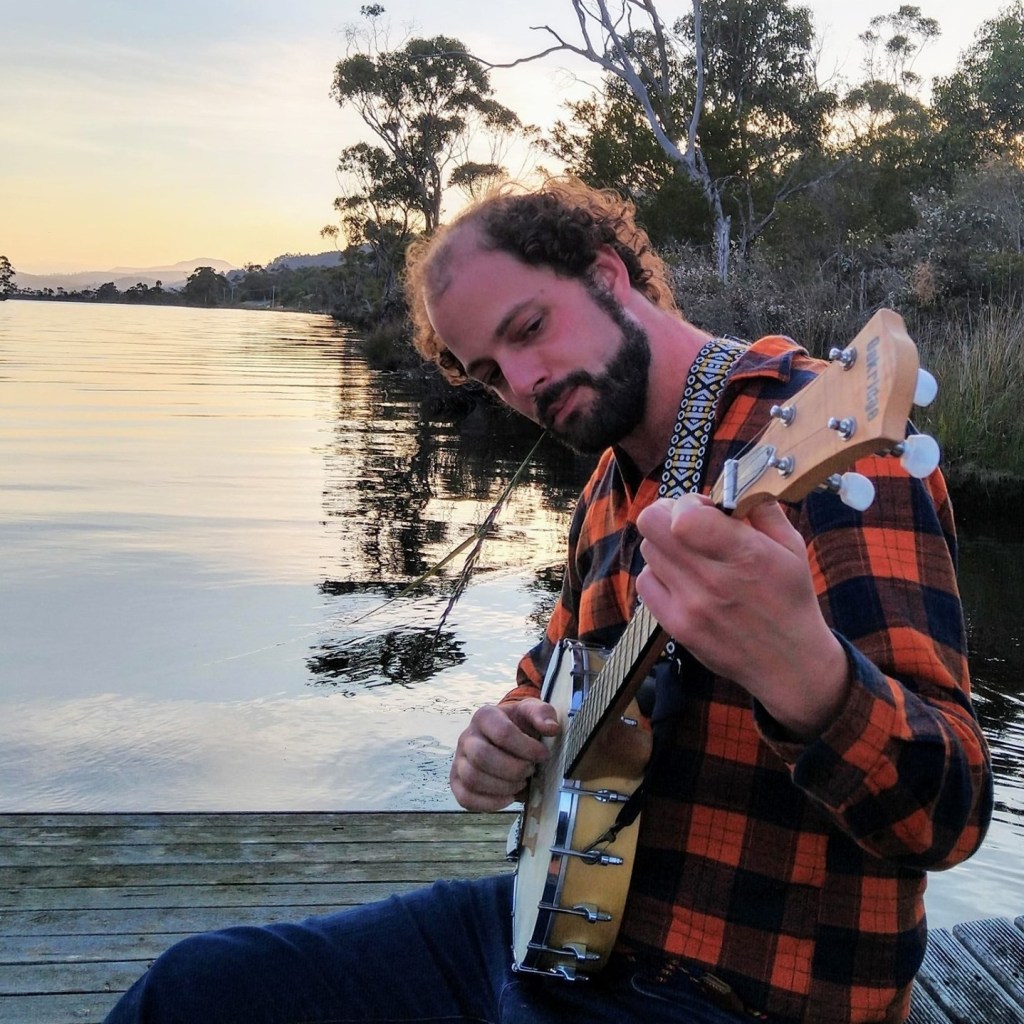 James Furlaud playing a guitar on the water with trees in the background