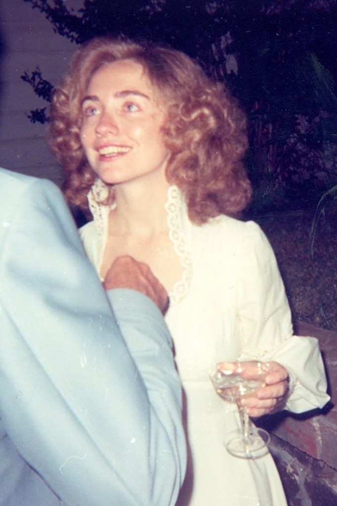 Hillary Clinton in a white dress, holding a glass, smiling at her wedding to Bill Clinton.