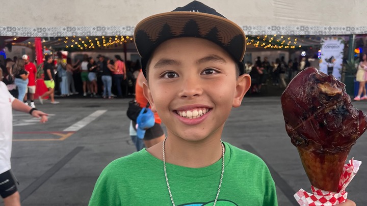 A smiling boy holds a turkey leg at a public event.