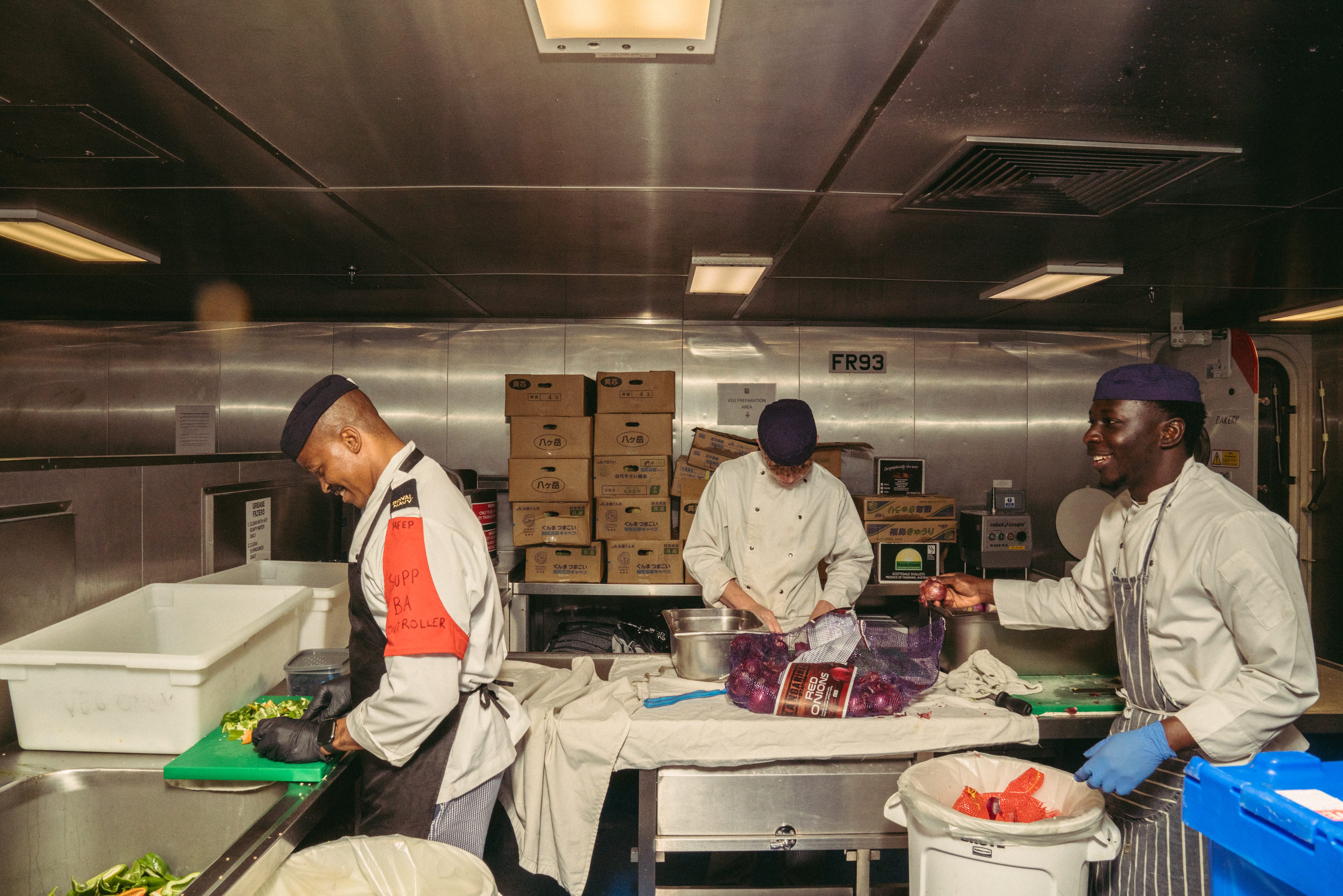 Royal Navy chefs chop vegetables and onions for dinner.