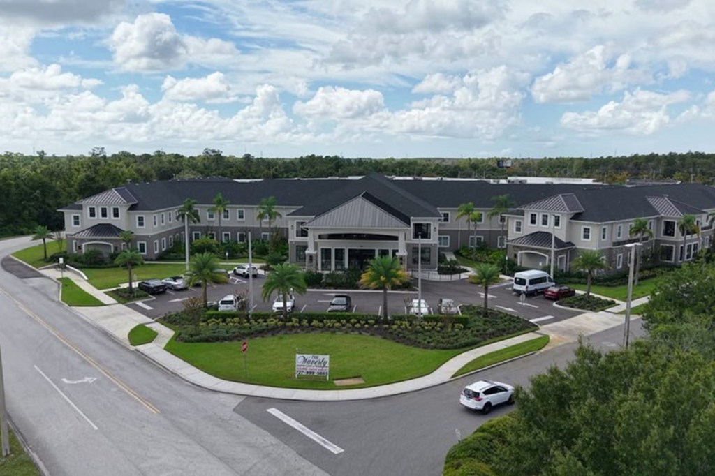 Aerial view of a large residential building with parking lots and palm trees, surrounded by dense forest.