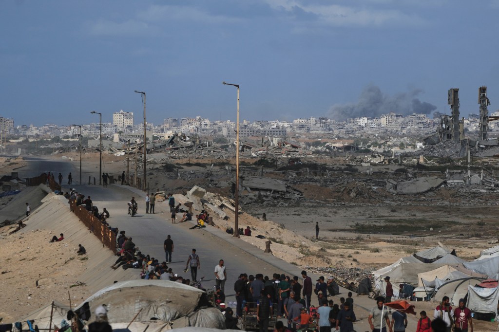 Displaced Palestinians on a coastal road near Wadi Gaza attempting to return to Gaza City, with destroyed buildings and tents visible in the background and foreground.