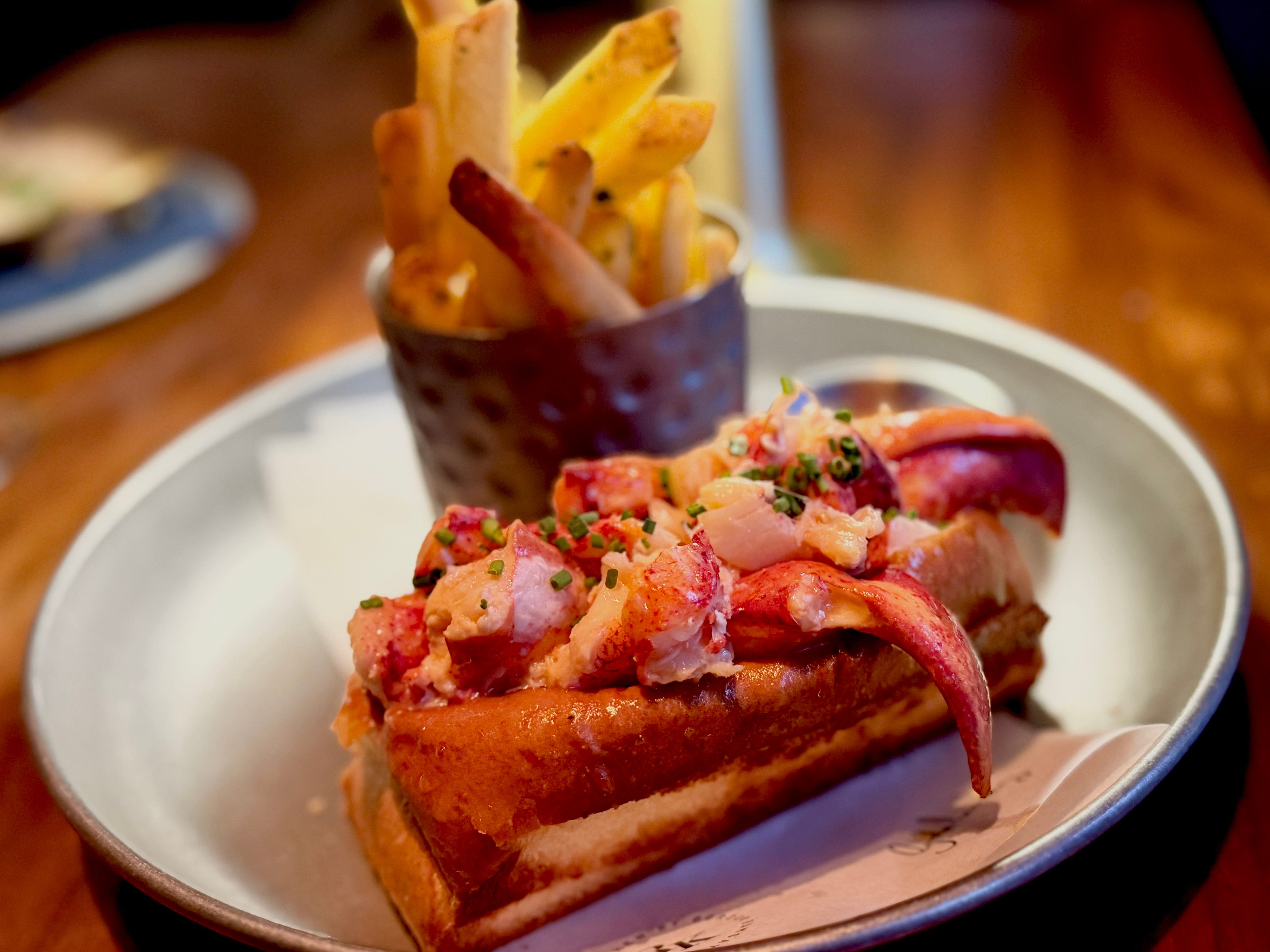 A lobster roll plated with a cup of french fries.