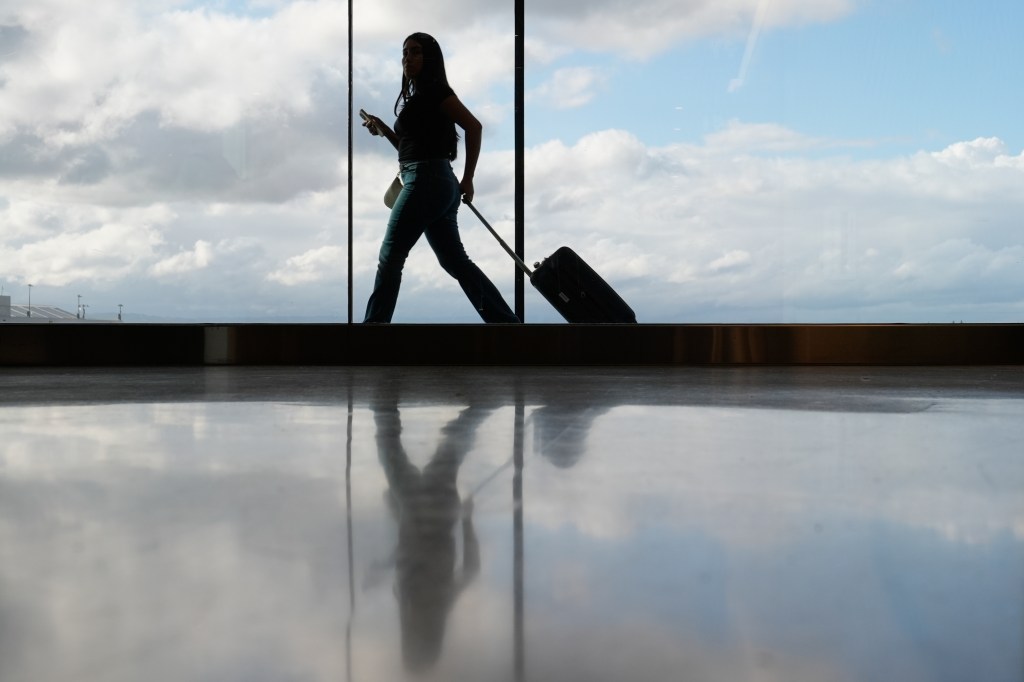 A traveler walks down a hallway with luggage at the Portland International Airport.
