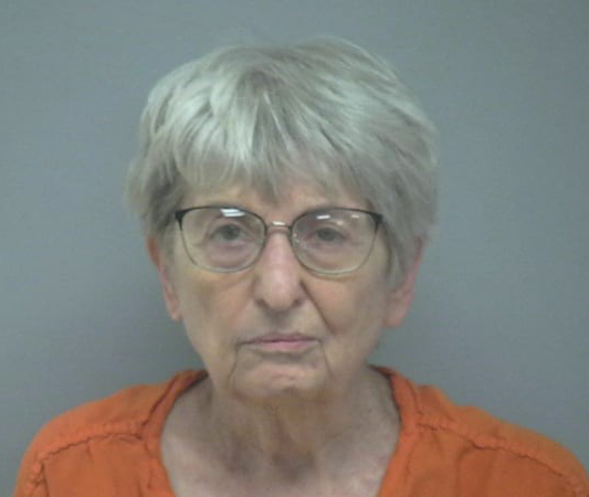 Mugshot of Harriet Kay Recker, an 82-year-old woman with short gray hair and glasses, wearing an orange jumpsuit.