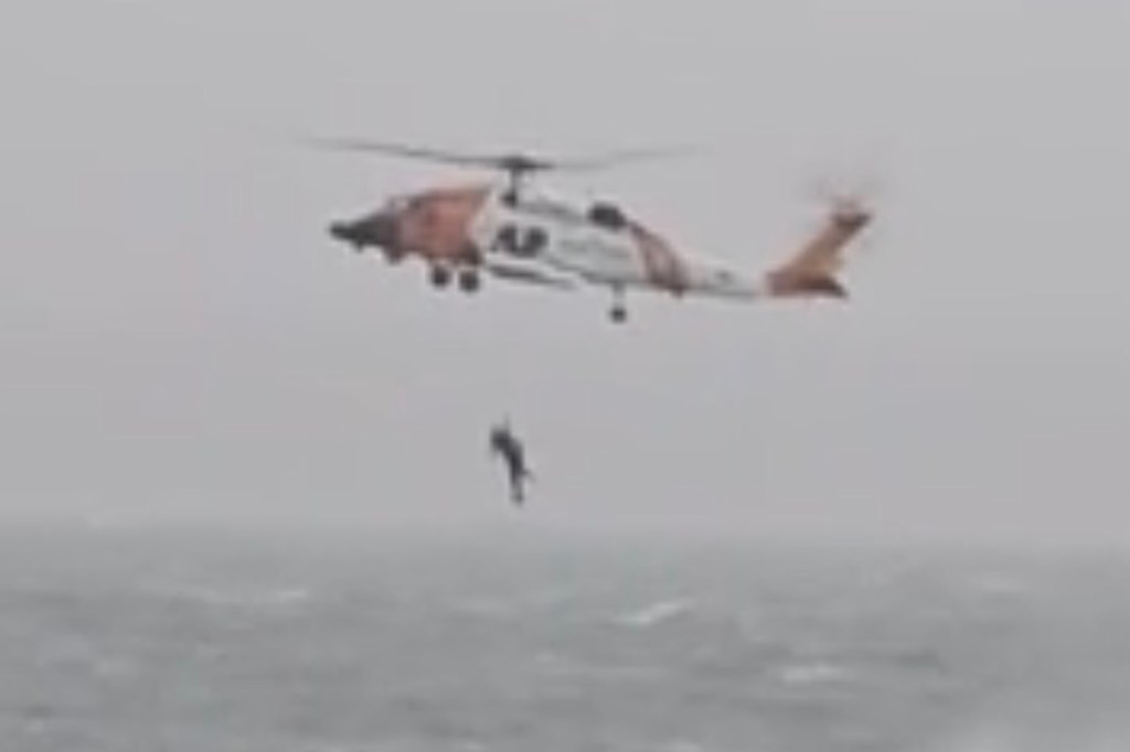 A US Coast Guard helicopter lowering a rescuer to the sea.