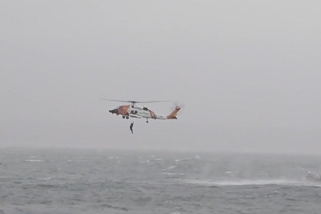 Coast Guard helicopter with a person being hoisted from choppy water.