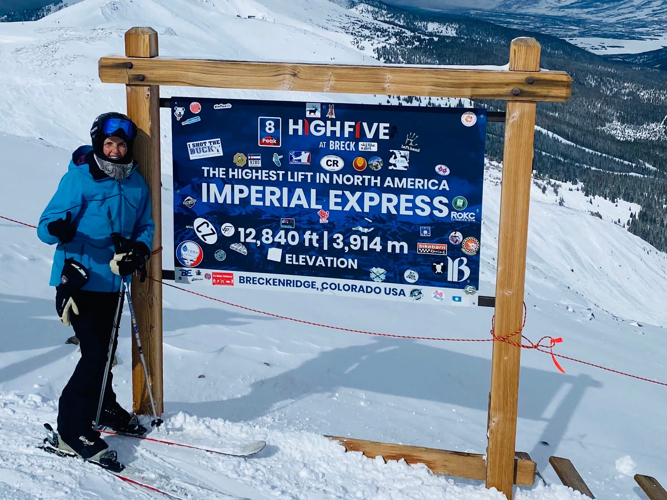 A woman standing next to a sign on a ski slope