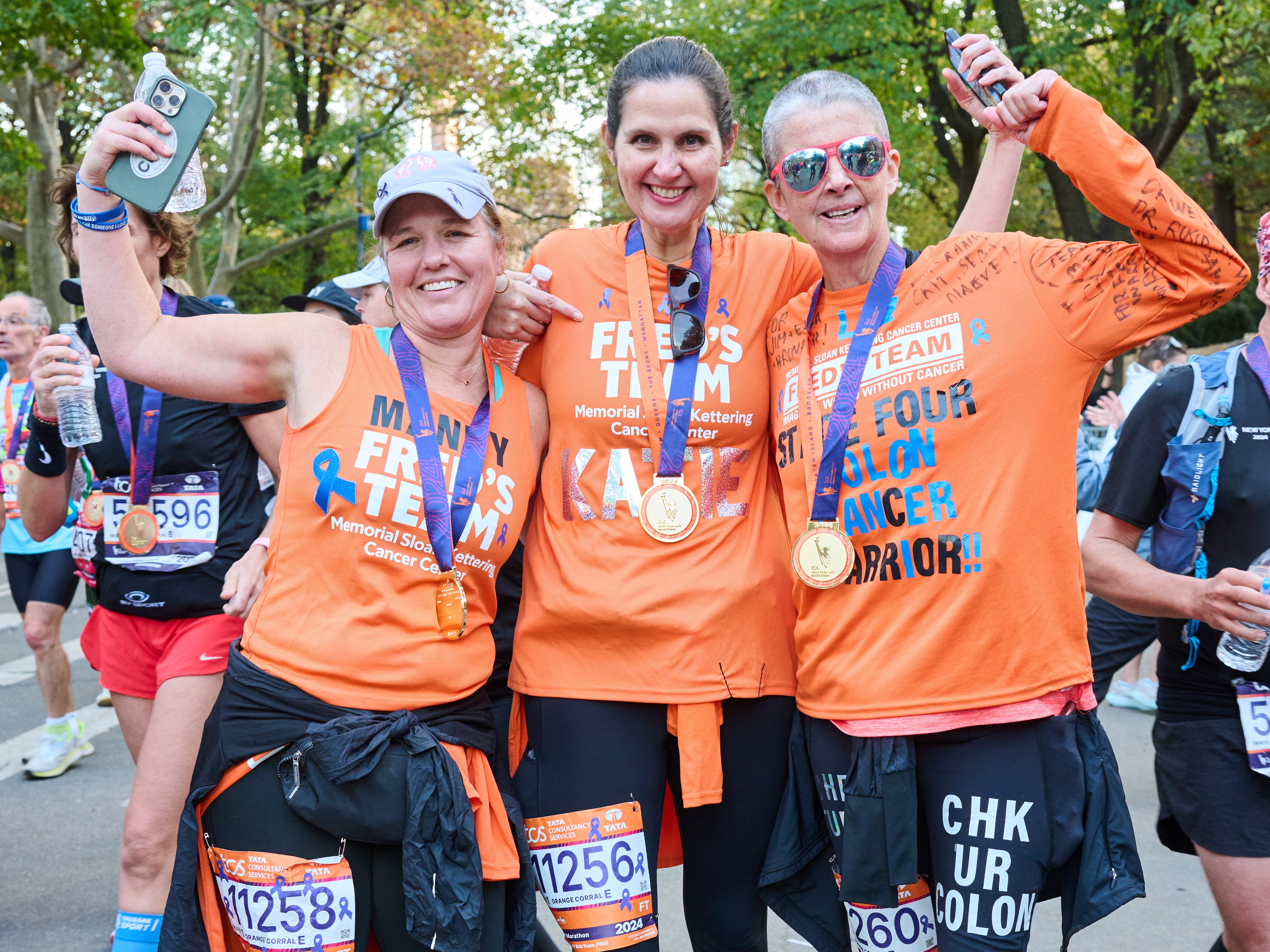 Three woman in orange T-shirts celebrating completing the New York City marathon