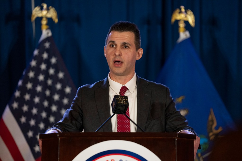 Michael Henry speaking at a podium with flags behind him.