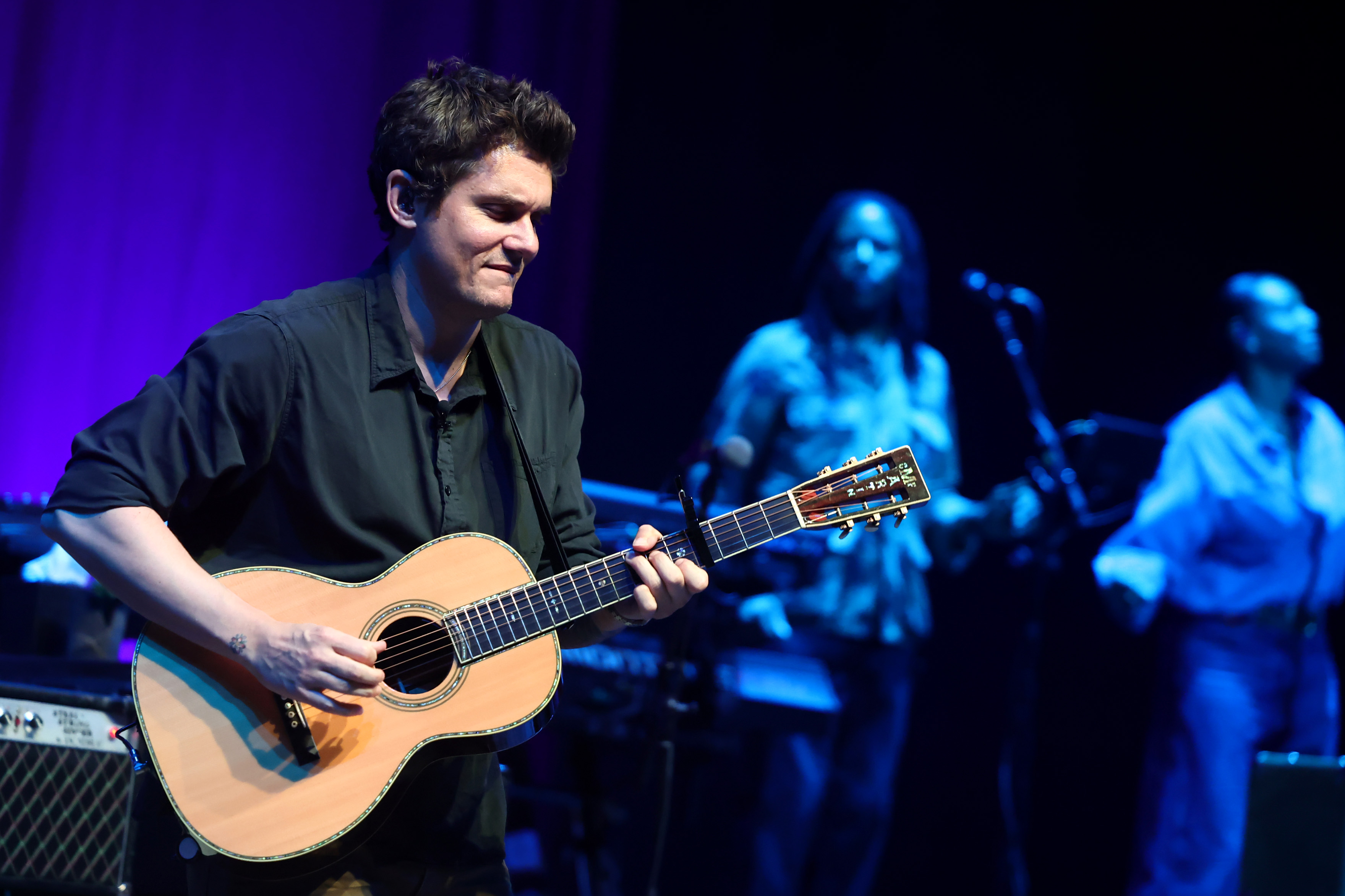 John Mayer performs on stage playing an acoustic guitar.