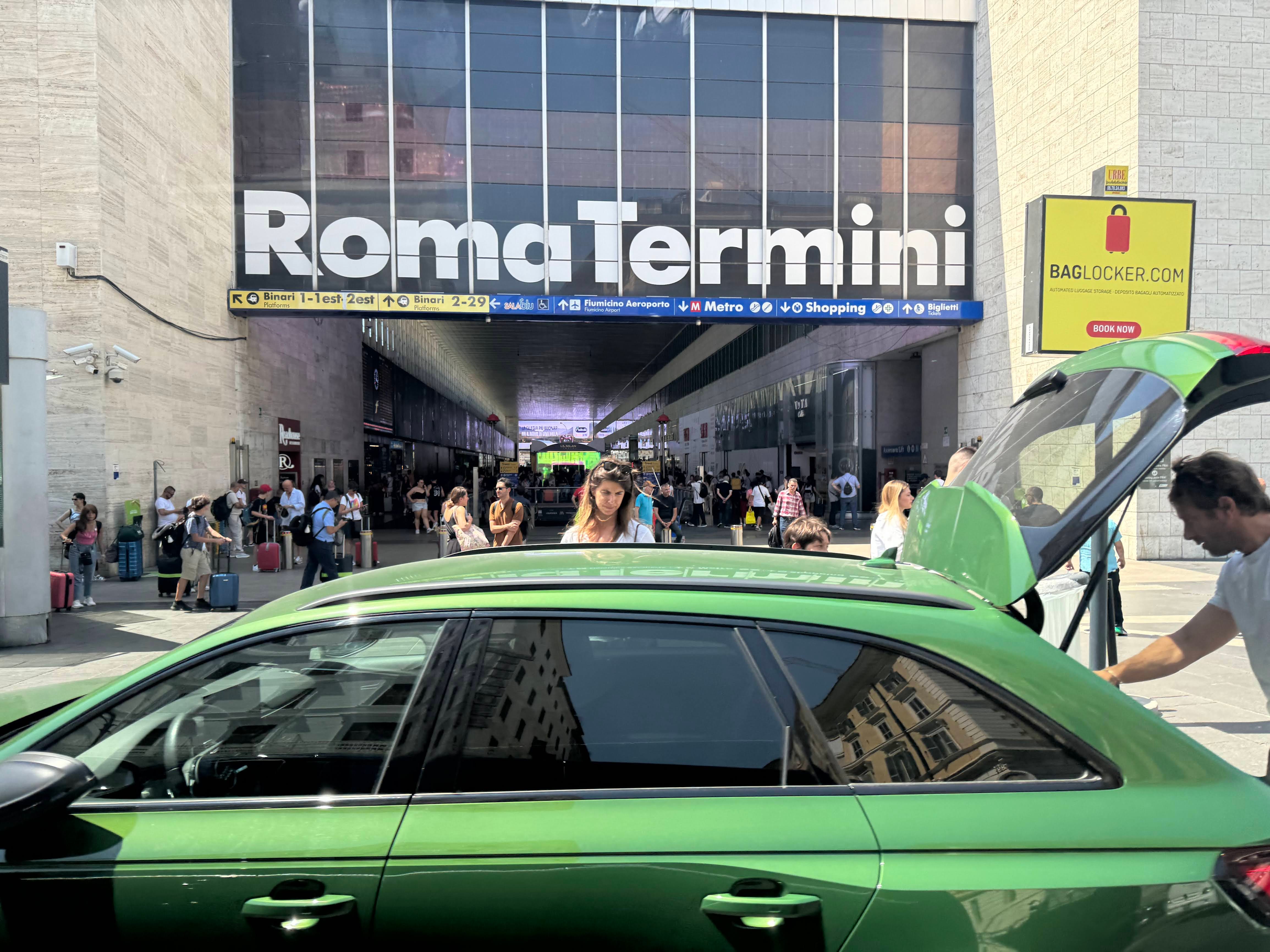 People milling about the Roma Termini train station in Rome, with someone unloading the trunk of their car.