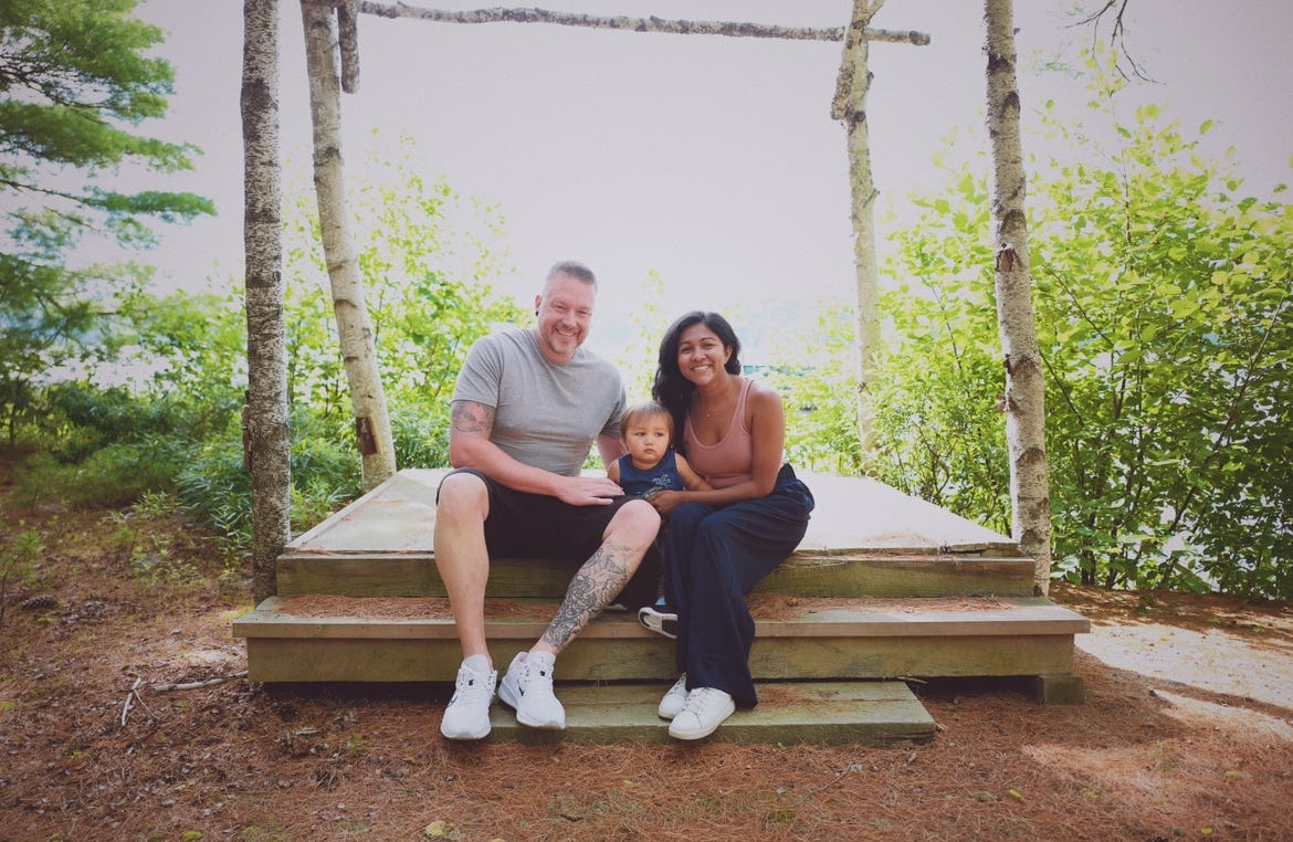 A husband and wife holding a baby on a park bench