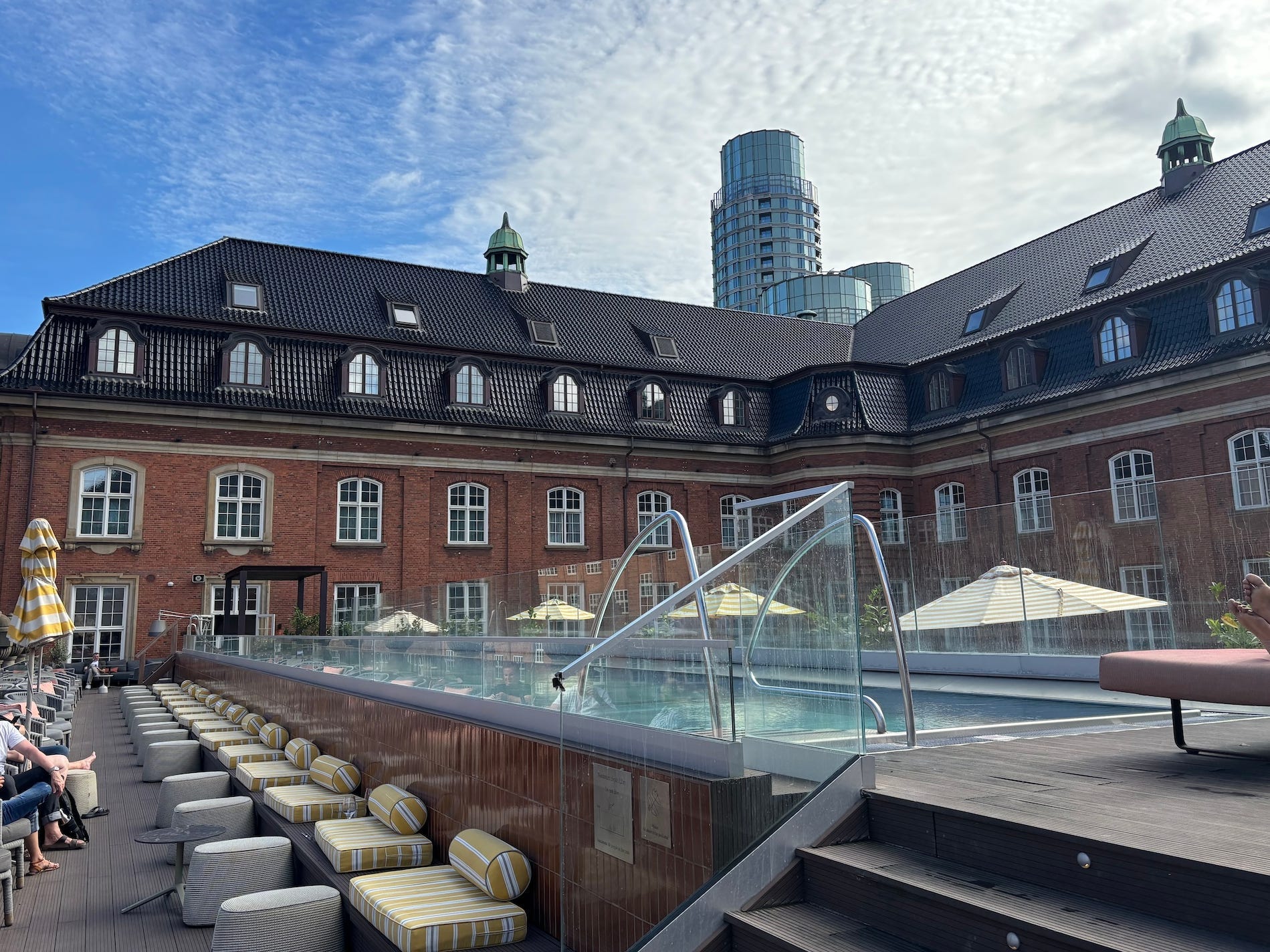 A rooftop pool at a hotel surrounded by brick and a partly cloudy sky.