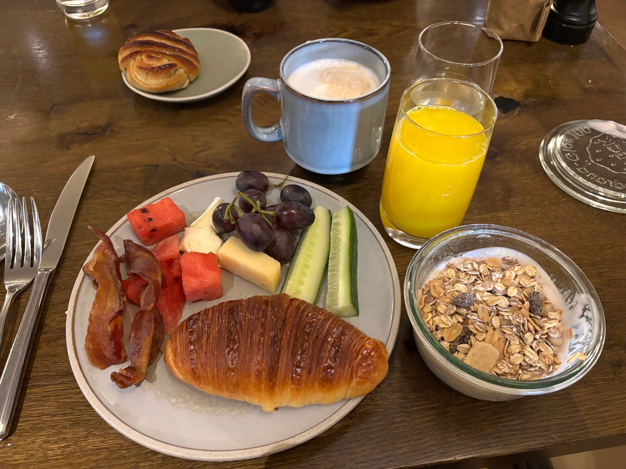A plate filled with breakfast foods, a bowl of yogurt, and a glass of organge juice next to a latte.