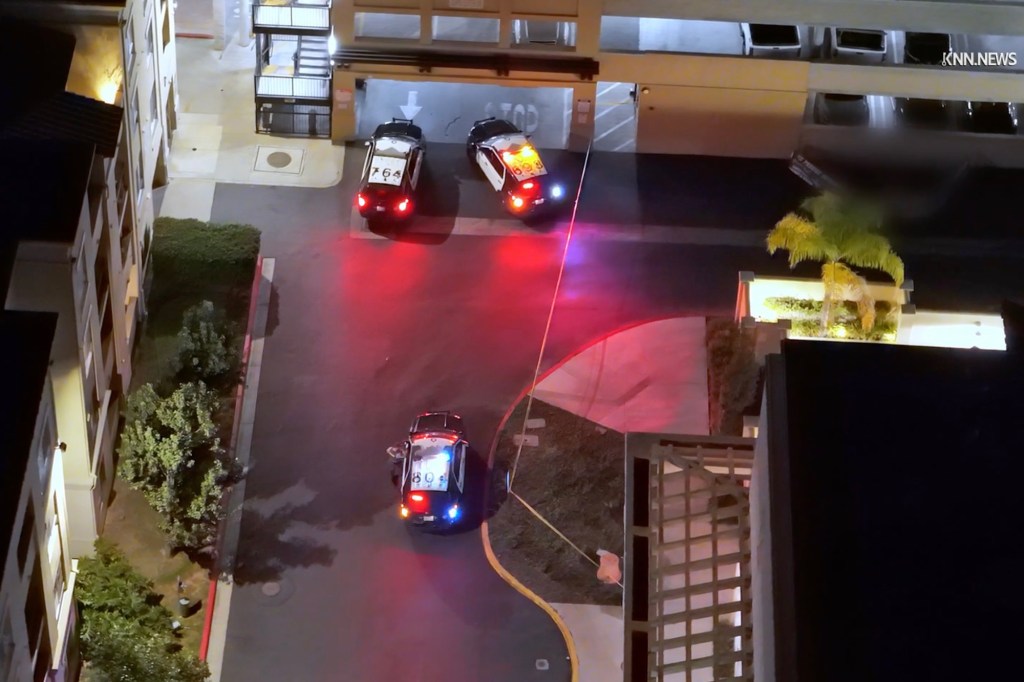 Aerial view of several police cars with flashing lights outside a multi-level parking garage at night.