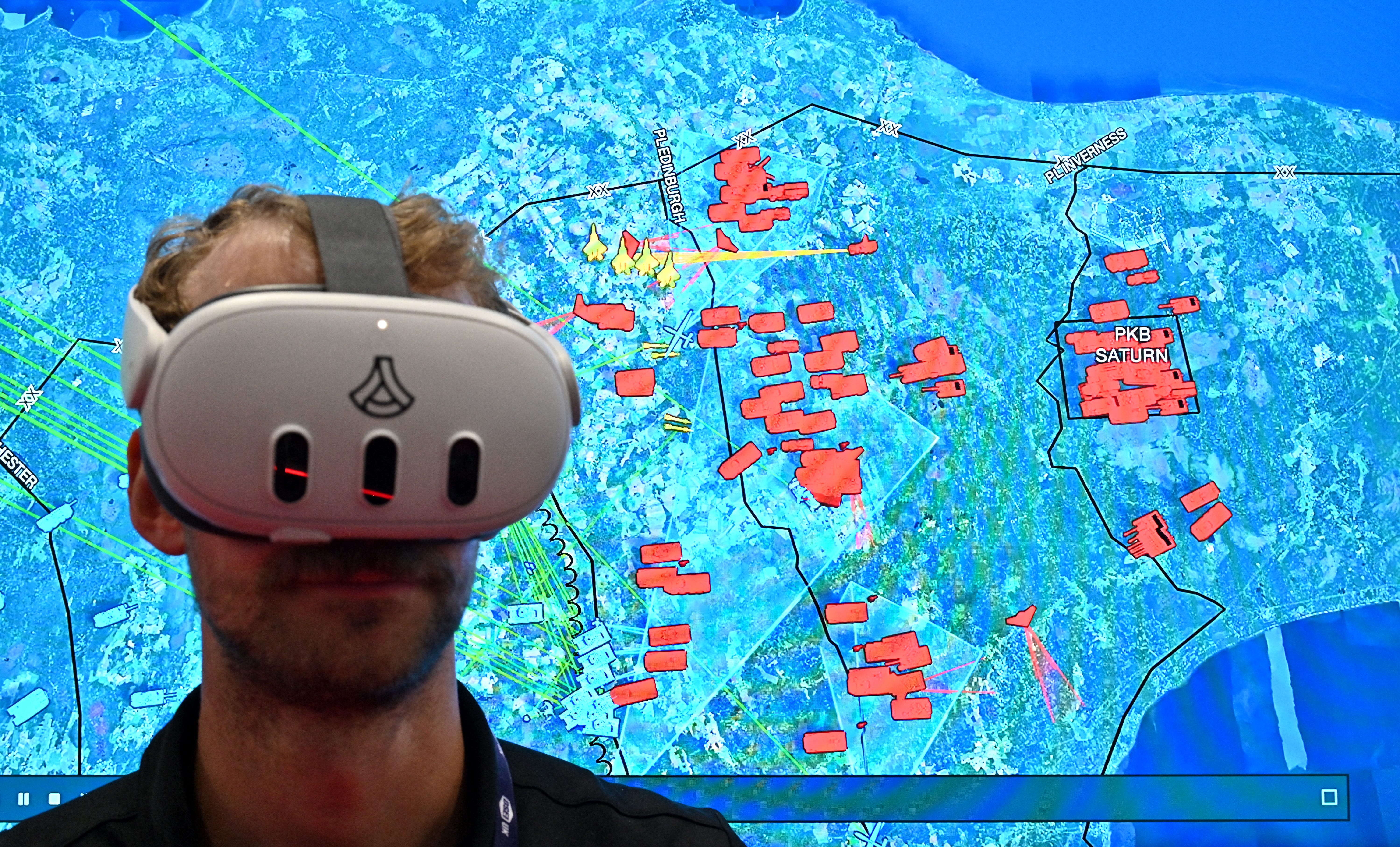 A man uses an Anduril VR headset with the Lattice software shown behind him on a screen.