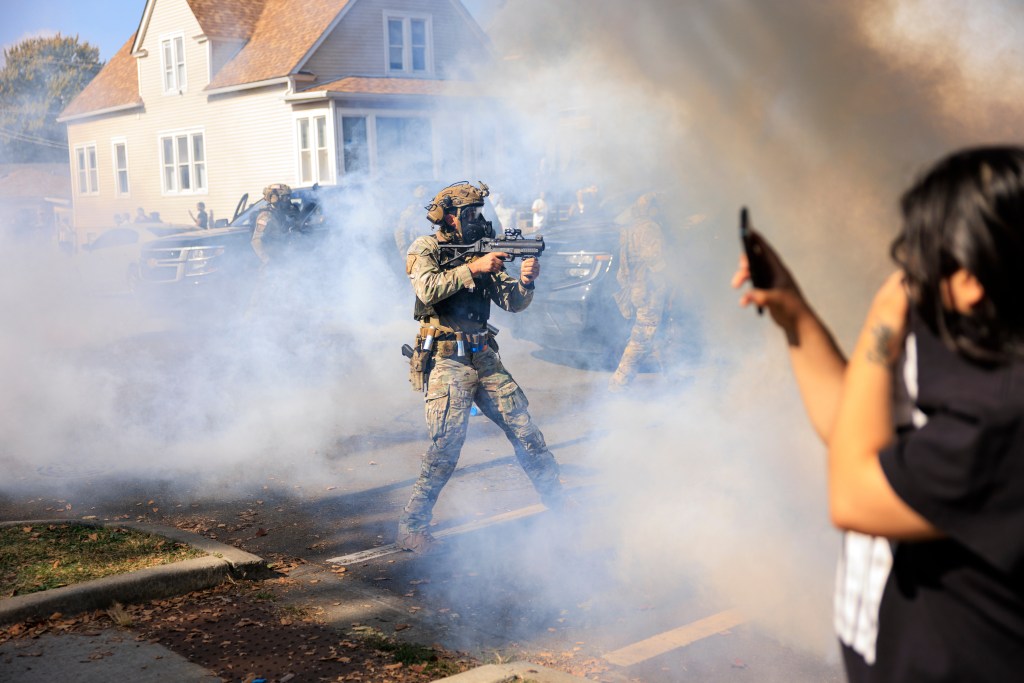 A U.S. Customs and Border Protection agent points a non-lethal weapon at protesters in East Side, Chicago.