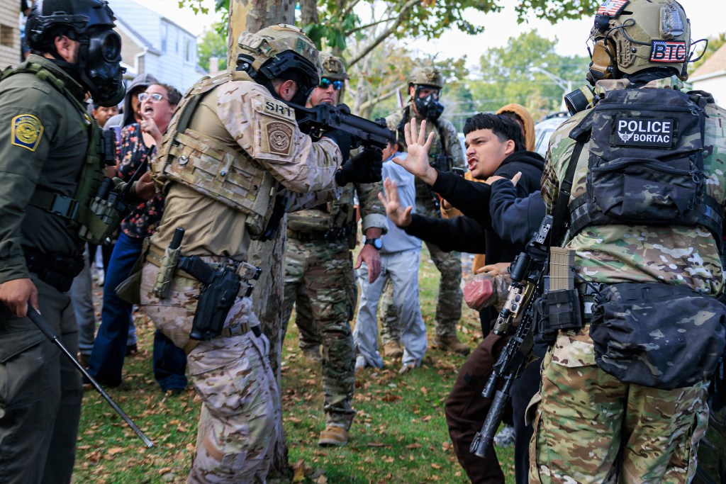 An ICE agent points a crowd control weapon at a protester.