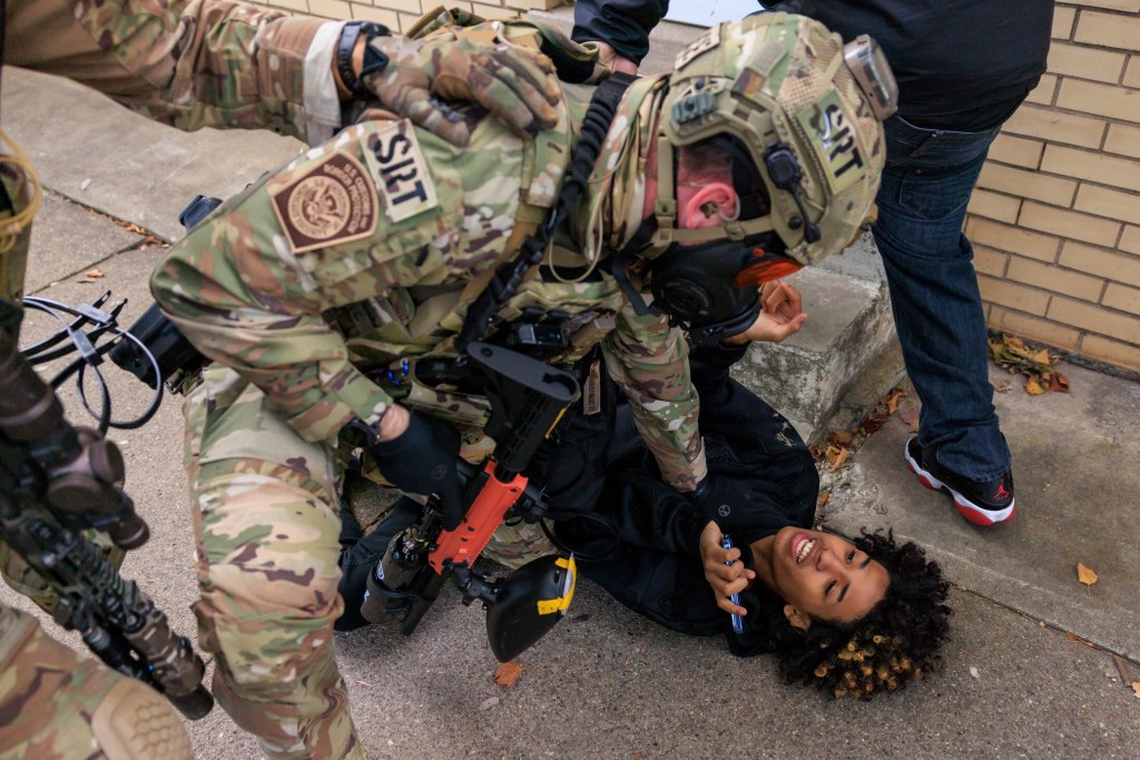 U.S. Customs and Border Protection agent detains a smiling protester, who is lying on the ground.