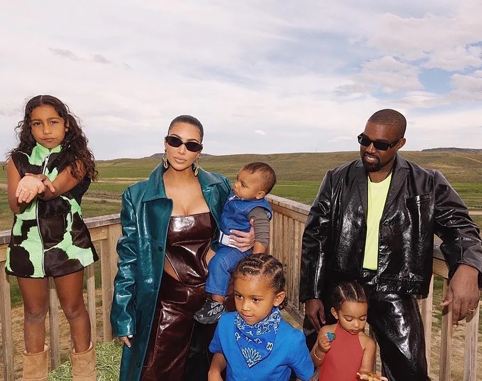 Kim Kardashian and Kanye West with their four children, North, Saint, Chicago, and Psalm, standing outdoors.