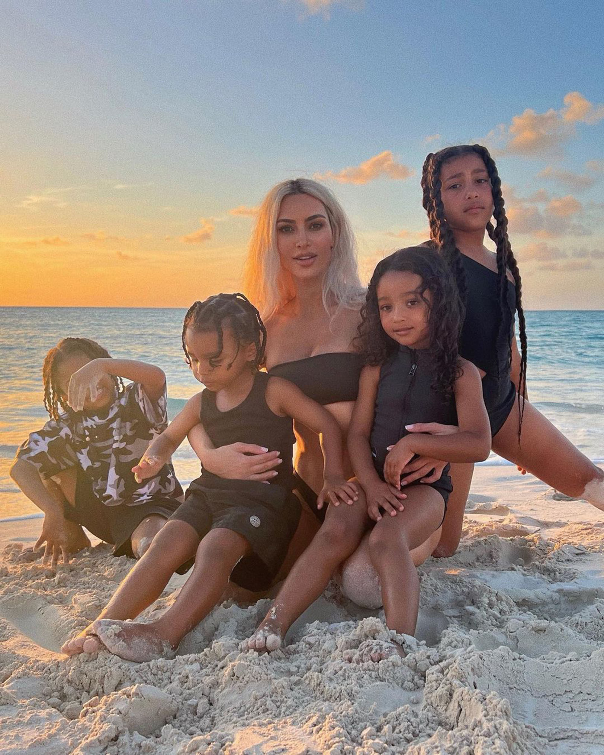Kim Kardashian and her four children posing on a beach at sunset.