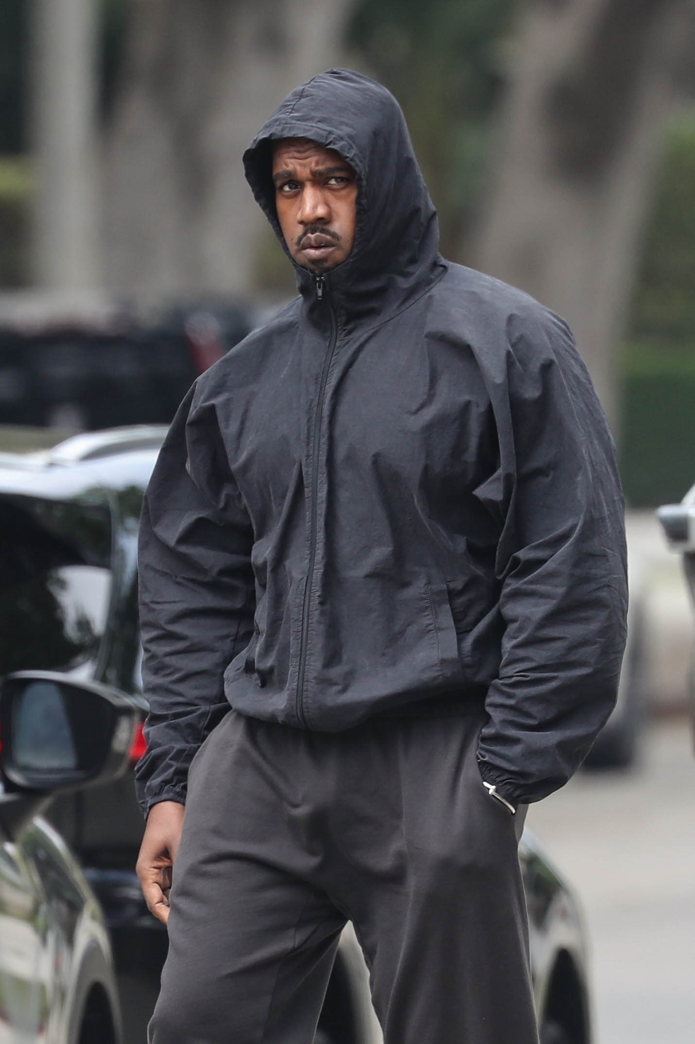 Kanye West in a black hooded jacket and dark pants.