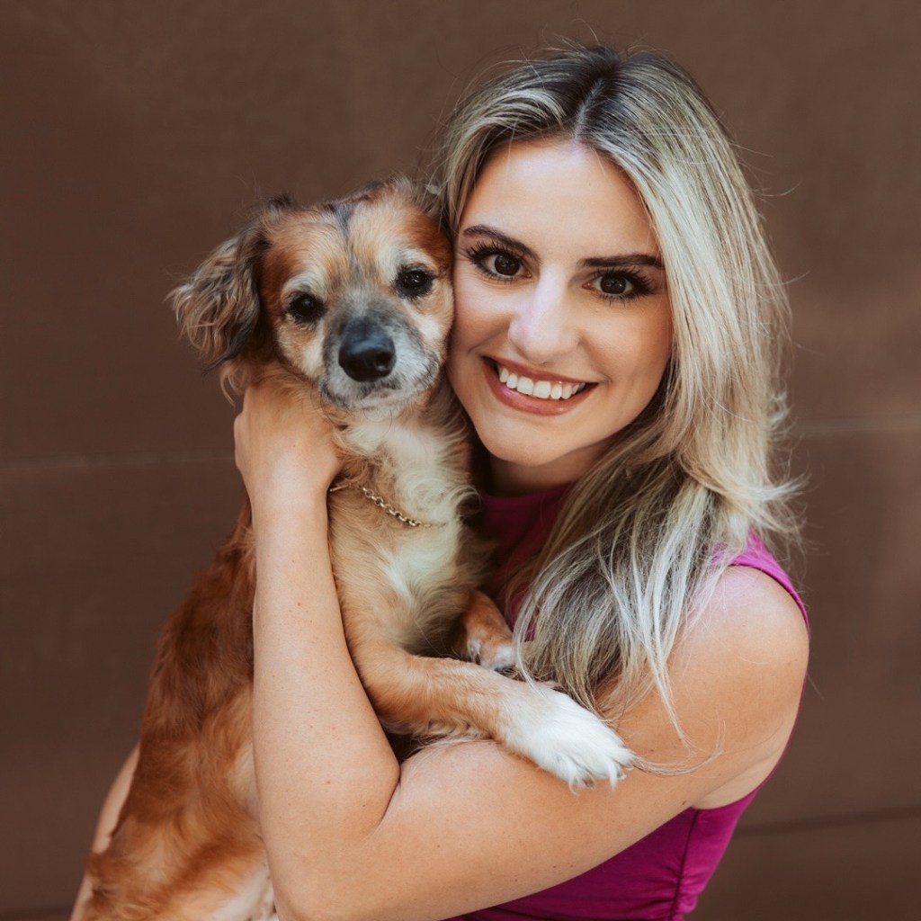 Woman smiling and holding a small brown dog.
