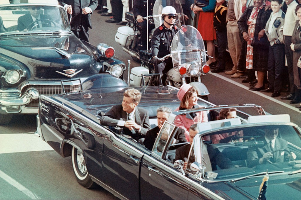 President John F. Kennedy and First Lady Jacqueline Kennedy smile in a motorcade in Dallas, Texas.