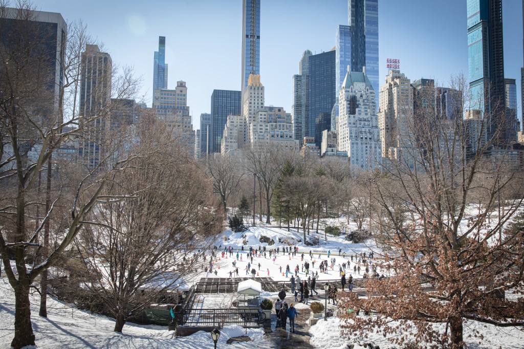 People ice skating at Wollman Rink in Central Park with New York City skyscrapers in the background.