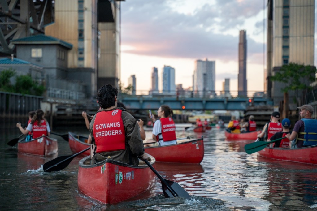 People canoeing on the Gowanus Canal with Manhattan in the background.