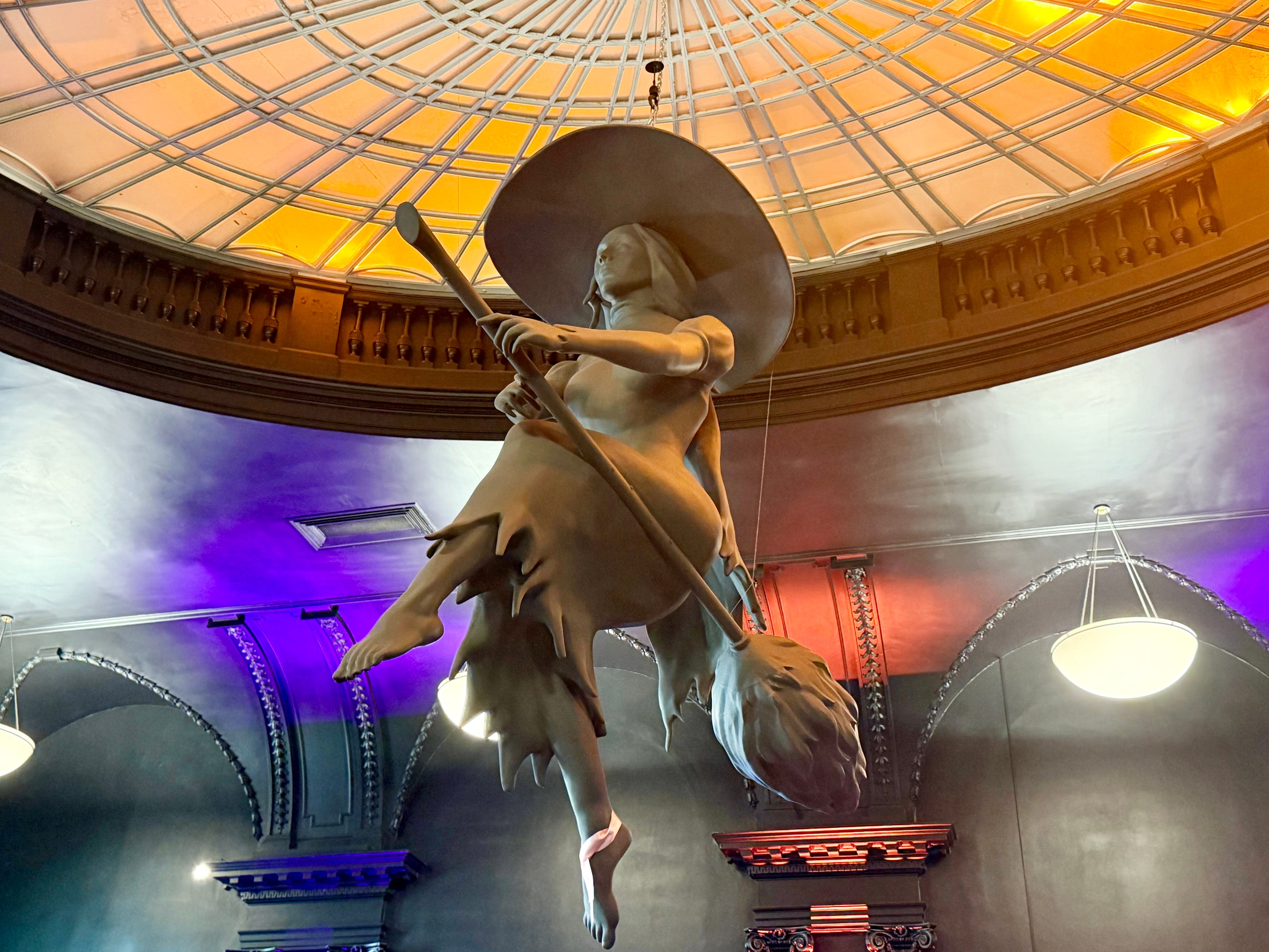 A witch statue hanging from a ceiling.