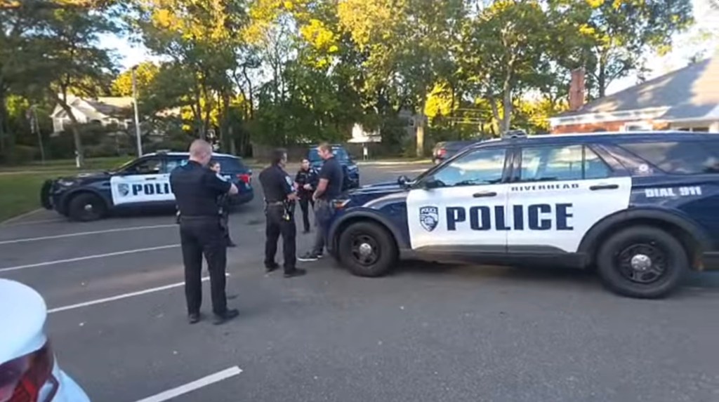 Two police cars and several police officers standing in a parking lot.