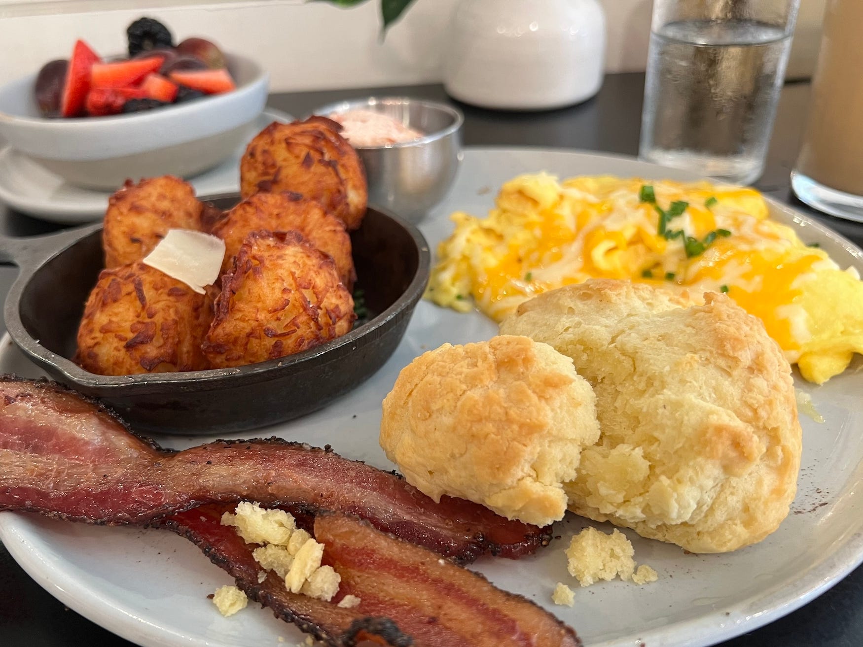A plate of breakfast food with bacon, eggs, a biscuit, and potatoes on it.