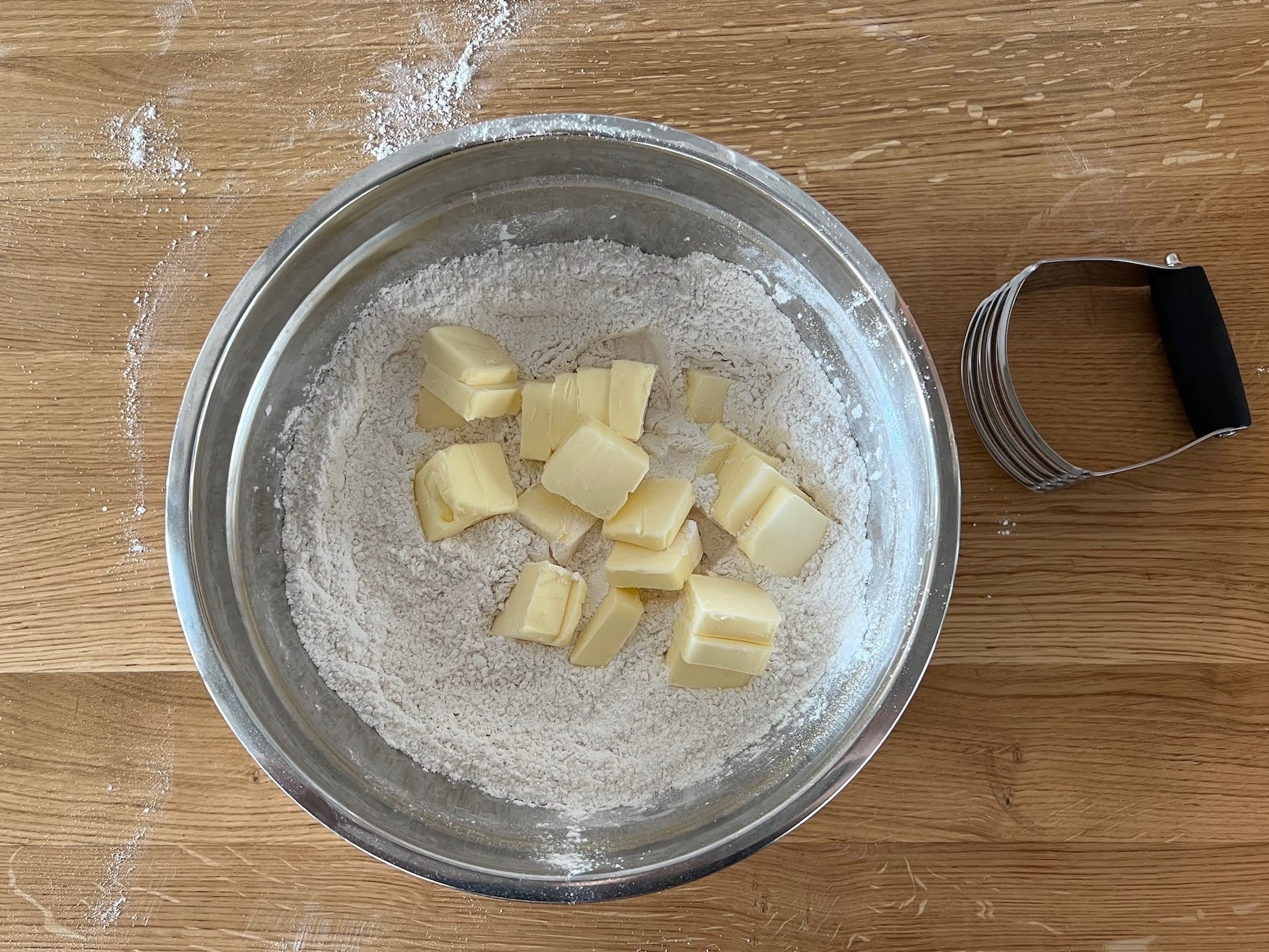 A bowl of flour and butter with a pastry cutter next to it.