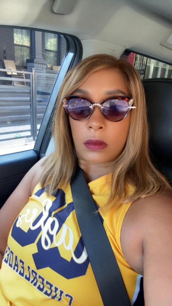 A woman wearing a yellow top, sunglasses, and seatbelt while in a car.