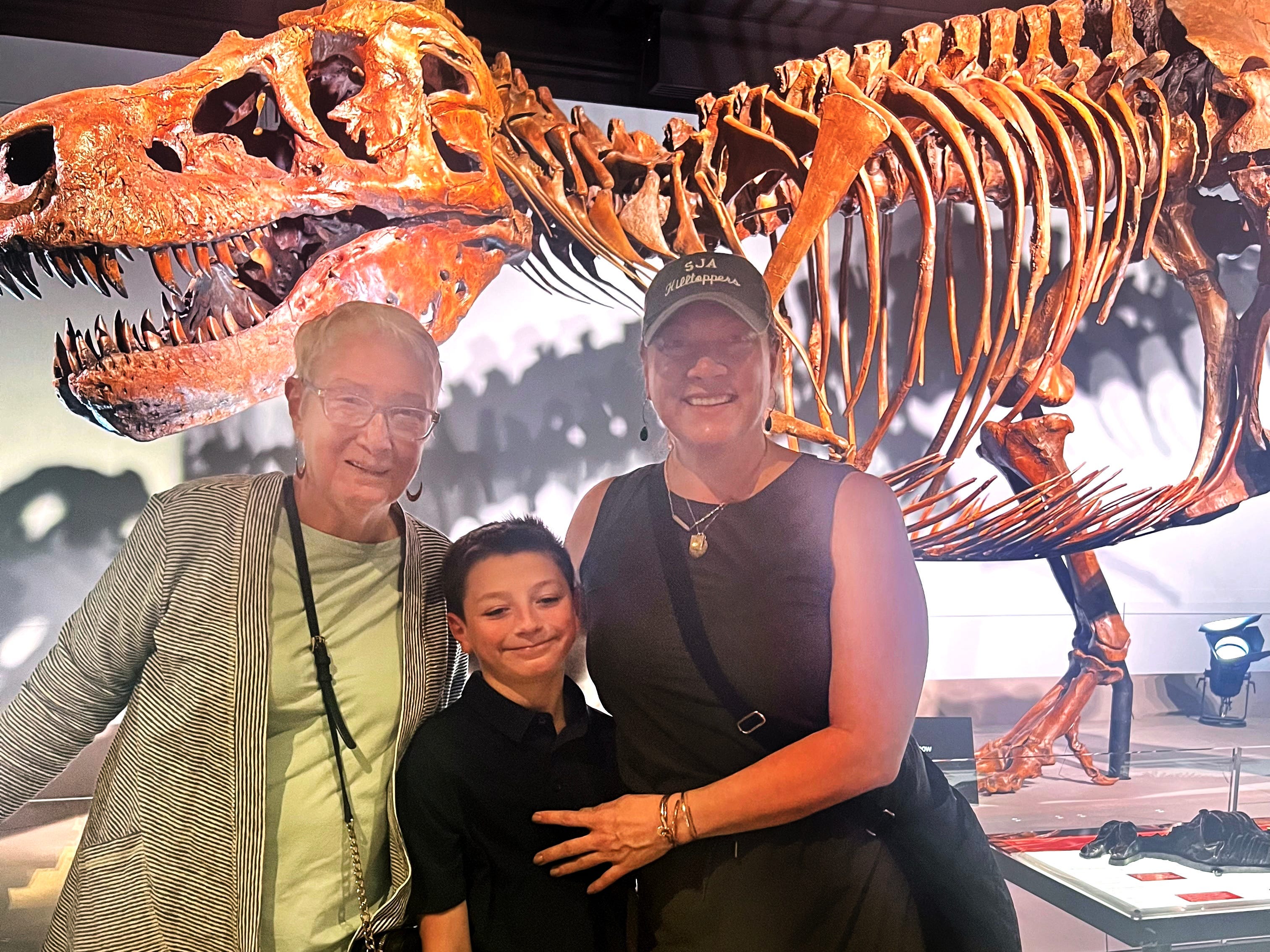 A grandmother, her daughter, and her grandson standing in front of a dinosaur exhibit