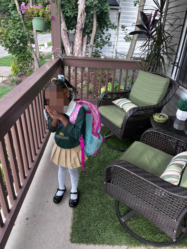 A young girl in a school uniform and backpack standing on a porch.