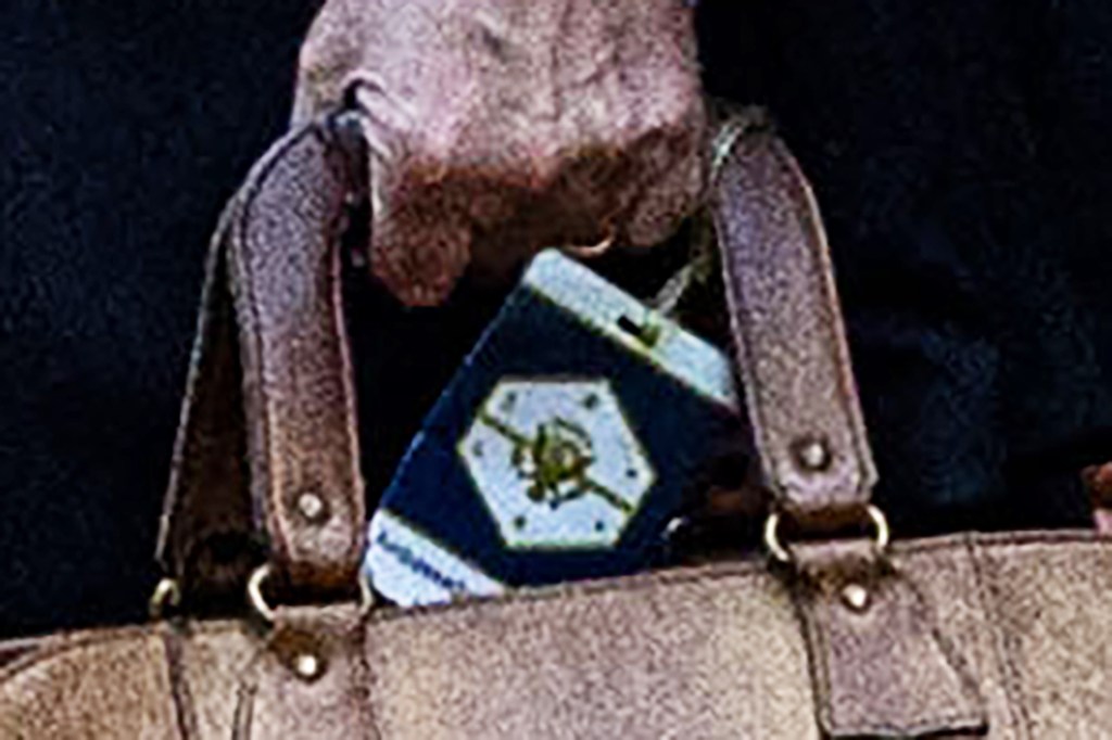 A White House pass with a logo of an eagle and shield hangs from a brown bag.