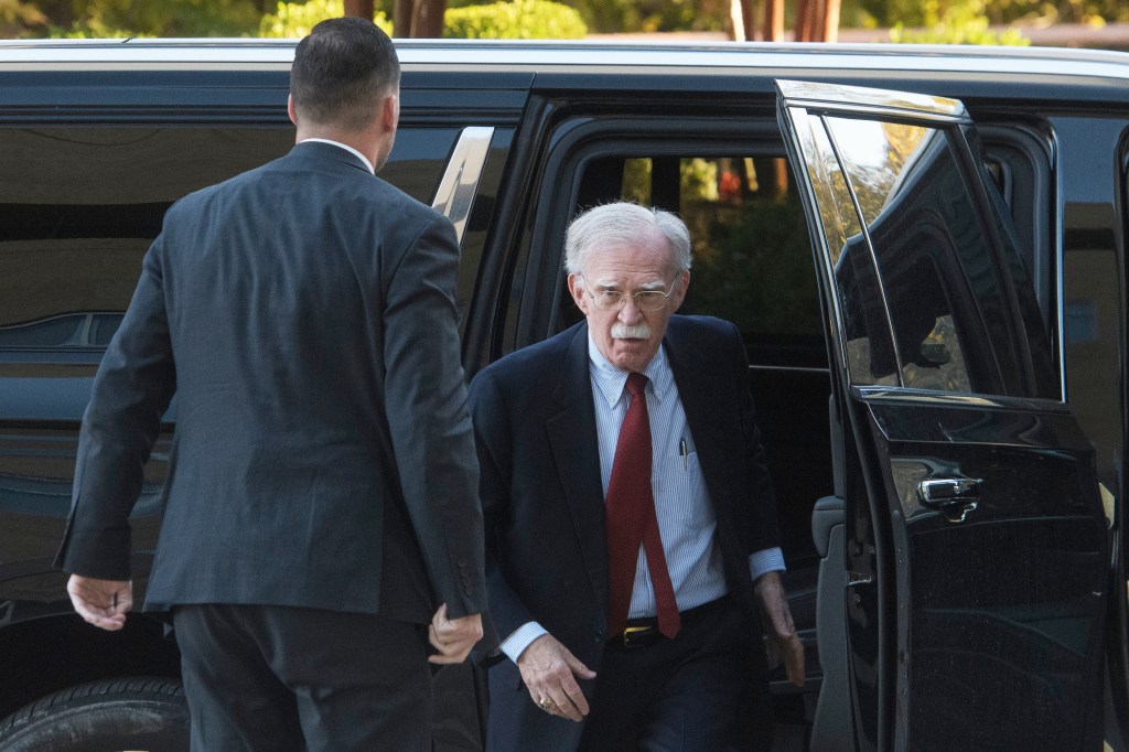 John Bolton exiting a vehicle, assisted by a man in a suit.