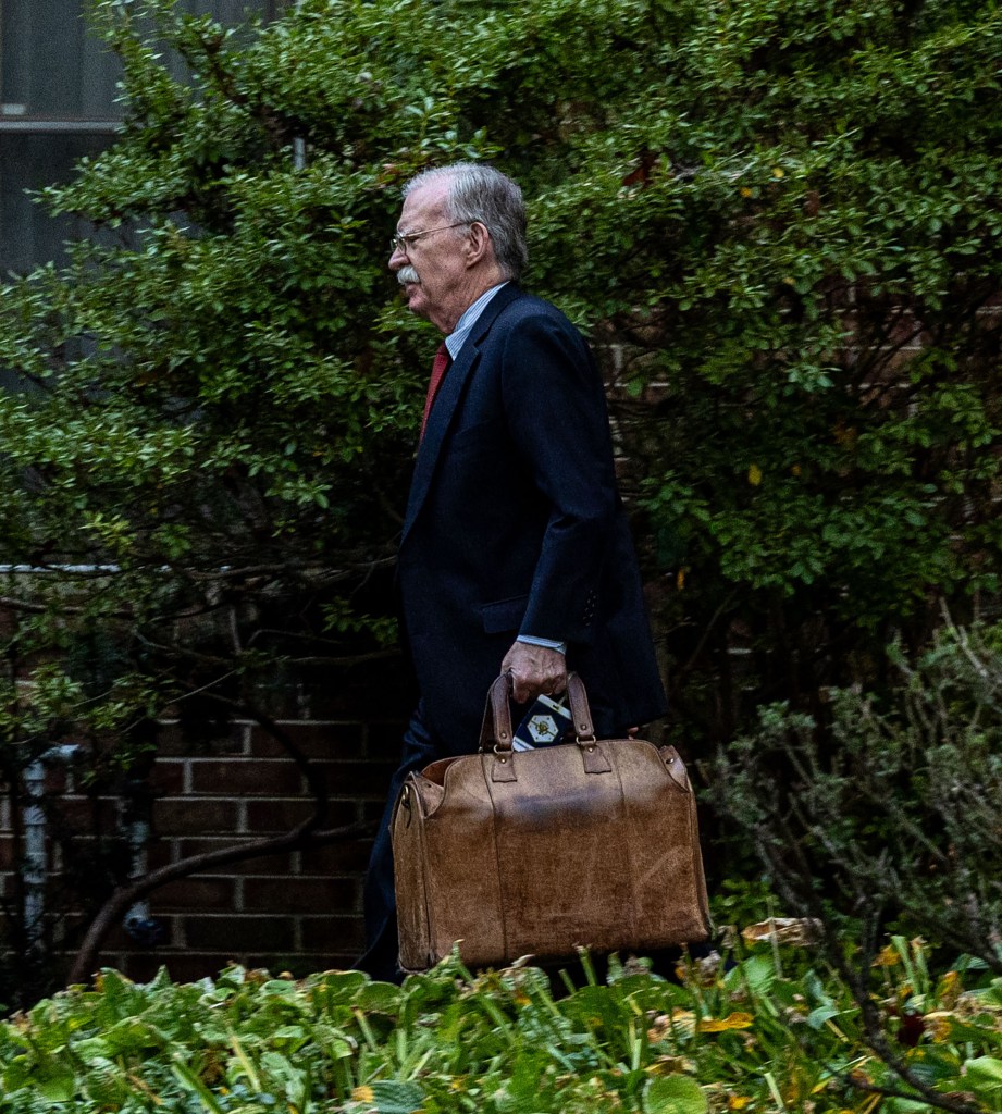 John Bolton walking while carrying a brown leather bag.