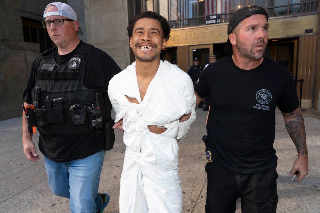 David Mazariegos, a man in a white paper-like suit, is escorted by two officers.