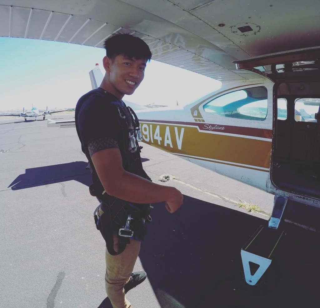 Man in skydiving harness standing by a small plane.