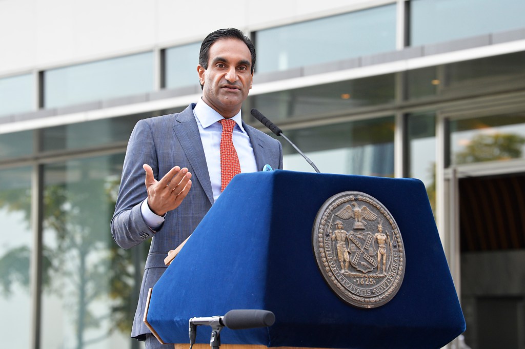 Dr. Jay Varma speaking at a podium with the New York City seal.