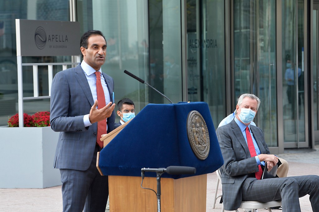 Dr. Jay Varma speaking at a podium while NYC Mayor Bill de Blasio listens, announcing the opening of Alexandria Labs for Covid-19 testing.