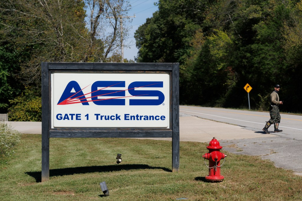 Signage for Accurate Energetic Systems (AES) at Gate 1, with a person walking down the road in the background.