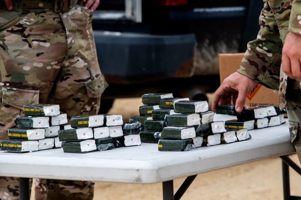 C4 explosives sit on a table, with a hand placing another block on the pile.