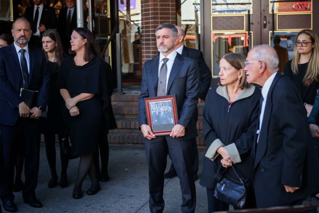 Mourners standing outside St. Dominic Roman Catholic Church in Brooklyn, with one man holding a framed photo of Nicola Tanzi.